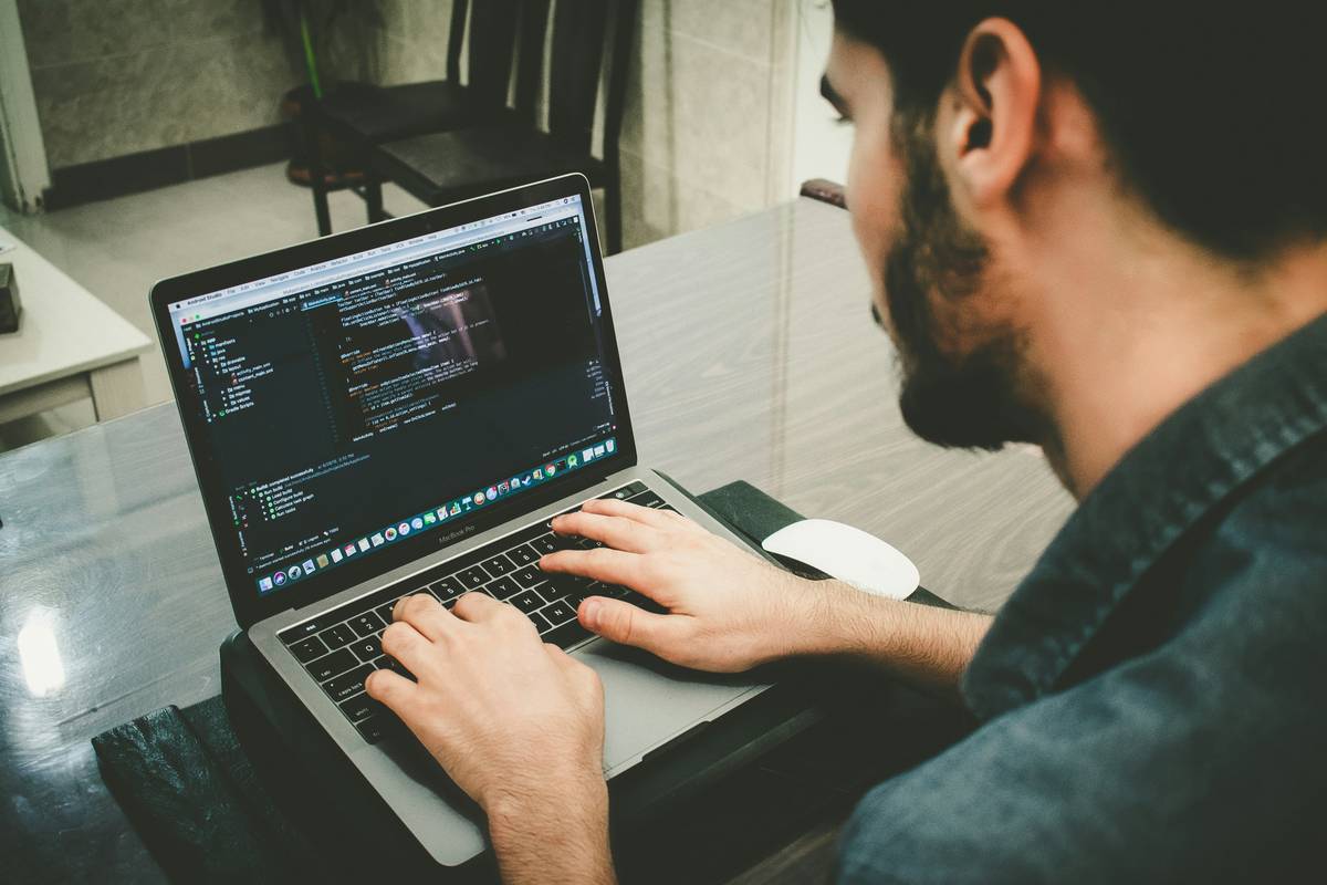 A beginner using a laptop to write robotics programming for beginners code that controls a small robotic arm in a simulated environment